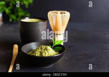 Tè e accessori da tè matcha verde biologico su sfondo nero. Cerimonia del tè giapponese. Cucchiaio Chashaku e frusta di bambù chasen per la produzione di ma Foto Stock