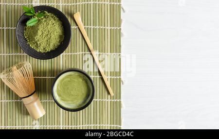 Accessori per tè e caffè matcha verde biologico su tappetino giapponese su sfondo di legno bianco. Cerimonia del tè giapponese. Cucchiaio Chashaku e chasen bamba Foto Stock