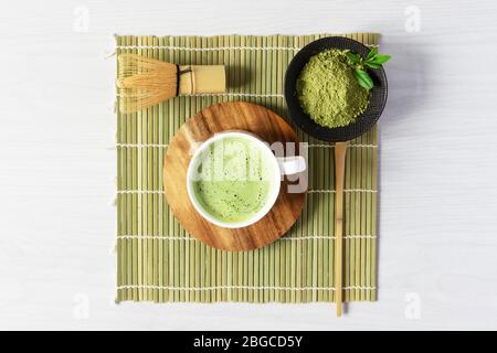 Accessori per tè e caffè matcha verde biologico su tappetino giapponese su sfondo di legno bianco. Cerimonia del tè giapponese. Cucchiaio Chashaku e chasen bamba Foto Stock