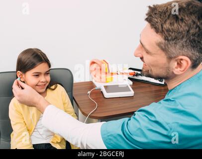Audiologo controllare un bambino ears.Mixed razza ragazza che ha prova di udito, procedura impedenza audiometria Foto Stock