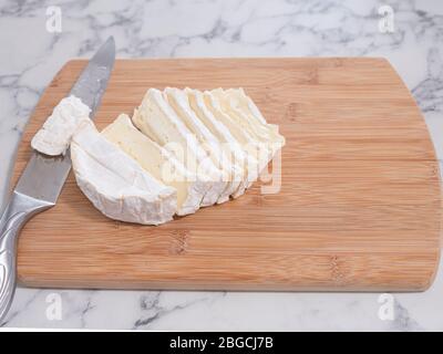 Formaggio Brie fresco affettato con un coltello su un tagliere in legno, superficie, piano in marmo. Foto Stock