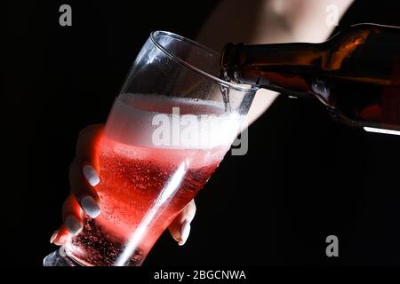 La ragazza con le unghie bianche si apre e versa un bicchiere di sidro/birra dalla bottiglia. Foto Stock