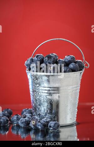 Mirtilli in un secchio di metallo primo piano su uno sfondo rosso. Cocktail multivitaminico. Stile di vita sano. Dieta estiva. Set di frutta . Giardino di mirtillo Foto Stock