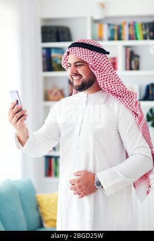 uomo arabo sorridente che parla a casa con una videoconferenza Foto Stock