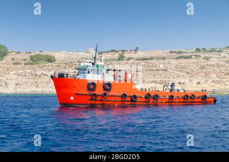 La barca a rimorchiatore con scafo rosso brillante va al mare Mediterraneo, l'isola di Malta Foto Stock