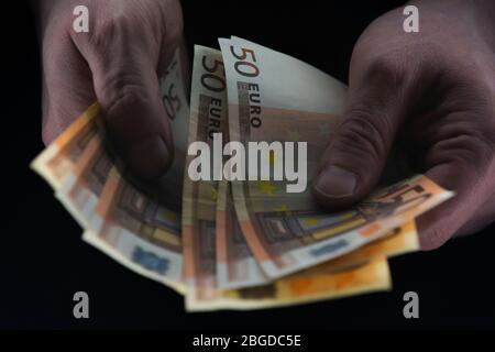 Uomo in possesso di 50 EURO fatture in una stanza buia, denaro illegale, concetto avidità. Foto Stock