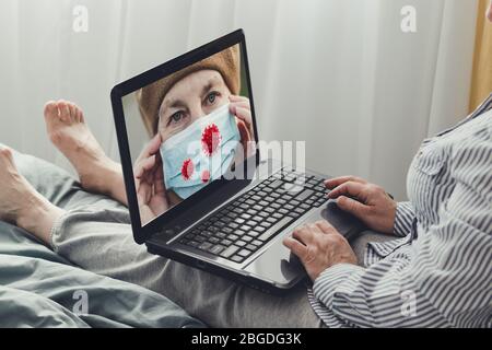 Donna adulta usa un laptop e guarda una notizia sul coronavirus e la protezione. Internet news, concetto di soggiorno a casa Foto Stock