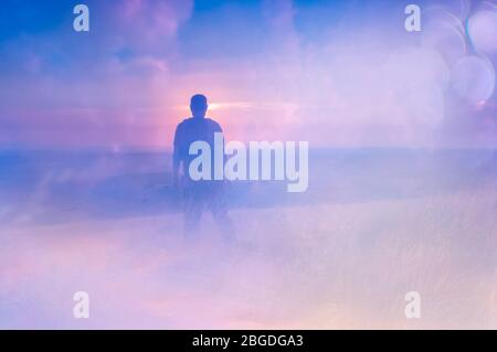 Una doppia esposizione di un uomo che guarda un tramonto dalla cima di una collina. Con un sogno astratto e sperimentale come edit. Foto Stock