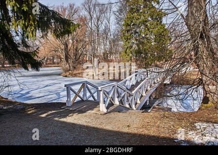 Un ponte con ringhiera in legno nella tenuta della famiglia Pushkin. Lo stagno è coperto di ghiaccio e neve. Il ponte ha una forma arcuata. Russia Foto Stock