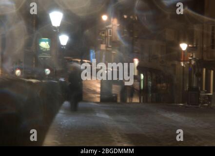 Un'immagine suggestiva di persone catturate in forte pioggia in un'area pedonale di notte con luci di strada che emettono un bagliore inquietante Foto Stock