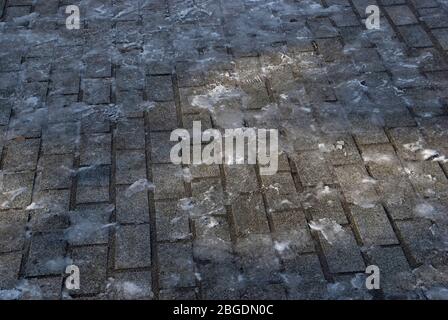 Pavimentazione stradale in inverno con un sottile strato di ghiaccio e impronte e una piccola piscina di luce Foto Stock