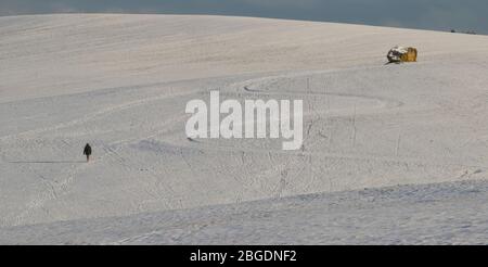 Scenario di paesaggio innevato con una figura solista lontana che attraversa la neve verso un grande monumento in pietra con un percorso curvilinoso anche visibile Foto Stock