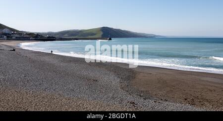 Aberystwyth, Ceredigion, Galles, Regno Unito. 21 Aprile 2020 Regno Unito Meteo: Quasi spiaggia vuota con cielo blu e sole come una persona cammina un cane lungo la spiaggia sud di Aberystwyth, come da linee guida del governo di esercizio quotidiano consentito. © Ian Jones/Alamy Live News Foto Stock