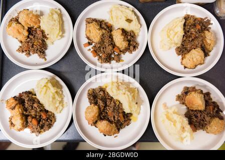 Una cena tradizionale britannica a scuola classica, manzo stufato, gnocchi e mash, che viene servita in un'organizzazione alimentare comunitaria in un villaggio hall Foto Stock