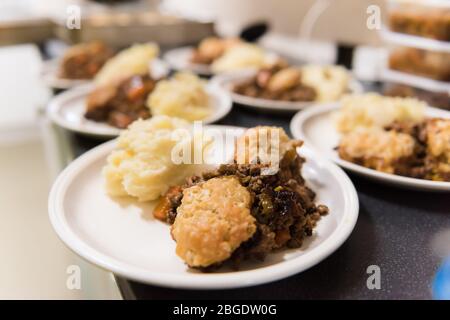 Una cena tradizionale britannica a scuola classica, manzo stufato, gnocchi e mash, che viene servita in un'organizzazione alimentare comunitaria in un villaggio hall Foto Stock