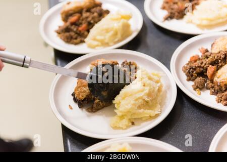 Una cena tradizionale britannica a scuola classica, manzo stufato, gnocchi e mash, che viene servita in un'organizzazione alimentare comunitaria in un villaggio hall Foto Stock