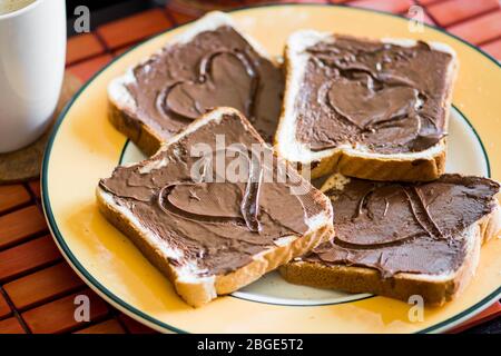 Fette di pane o pane tostato con crema di cioccolato e tazza di caffè e latte, forma a cuore Foto Stock