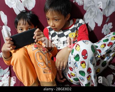 Un ragazzo gioca una partita su uno smartphone mentre il fratello sta guardando. Foto Stock