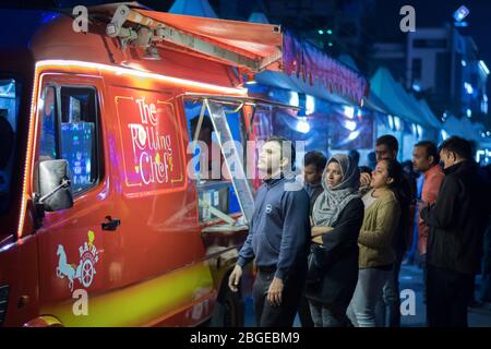 Un gruppo di persone che attendono fuori da un camion di cibo rosso per i loro ordini durante la notte Foto Stock