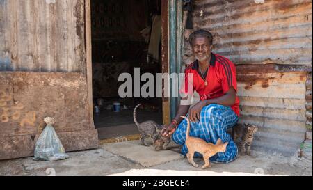 Un povero indiano con i suoi gatti e gattini di fronte al suo turno di lavoro shack in un baraccopoli Foto Stock