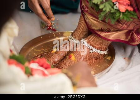 Primo piano dei piedi decorati di una sposa indiana mentre un rituale tradizionale si è esibito durante il matrimonio Foto Stock