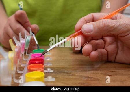 Mani di adulti e bambini che immerge un pennello in vasi di vernice acrilica di colori diversi su un tavolo di legno. Concetto di hobby Foto Stock