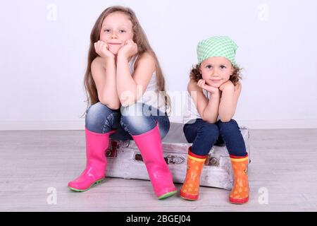 Belle ragazze piccole seduti su valigia su sfondo muro Foto Stock