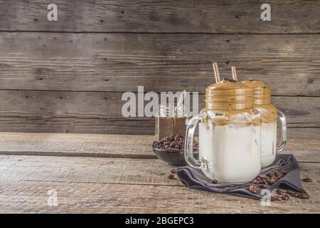 Drink alla moda, caffè dalgona. Bevanda a base di caffè istantaneo montata con latte freddo e zucchero. Bevanda cremosa e soffice al caffè montato, su un rustico backgroun in legno Foto Stock