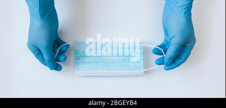 primo piano dei guanti per le mani del medico con una maschera per il viso medica per la protezione contro le infezioni. Stop Coronavirus Concept banner. Utilizzo della maschera facciale durante Foto Stock