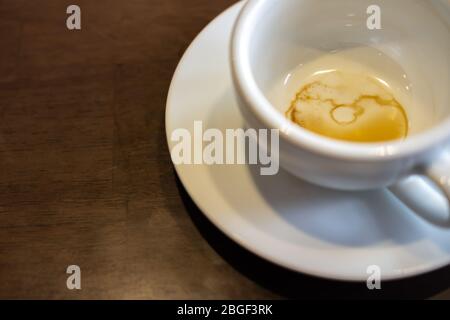 Primo piano. Macchie di caffè sul fondo di una tazza bianca con piattino sul tavolo di legno. Foto Stock