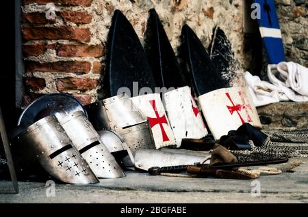 Armi medievali, scudi e caschi dall'epoca della crociata sul pavimento del castello durante una rievocazione storica Foto Stock