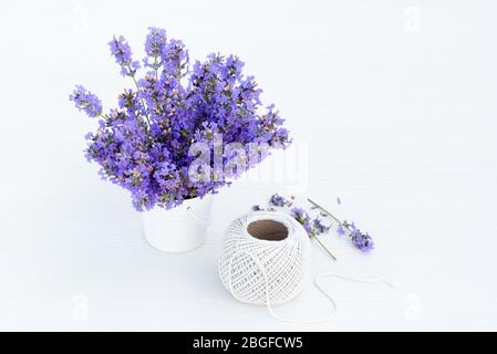 Lavanda fresca in piccolo secchio bianco e palla di canapa su sfondo bianco di legno. Foto Stock