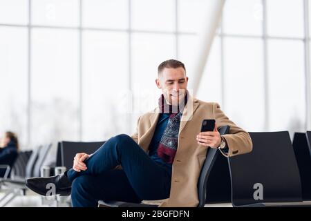 Giovane uomo di Occupato in attesa di partenza all'aeroporto mentre utilizzando il suo telefono Foto Stock