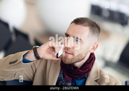 Bello hipster imprenditore moderno con la barba chiamando sul cellulare in aeroporto o edificio per uffici Foto Stock