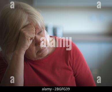 Donna depressa più anziana con la testa appoggiata su di lei hand.in un ambiente domestico. Foto Stock