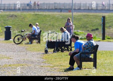 Wyke Regis, Weymouth, Dorset, Regno Unito. 21 aprile 2020. Meteo Regno Unito. Persone sedute sulle panchine al sole sul sentiero Rodwell a Wyke Regis a Dorset in un caldo pomeriggio soleggiato durante il blocco pandemico del coronavirus. Credito immagine: Graham Hunt/Alamy Live News Foto Stock