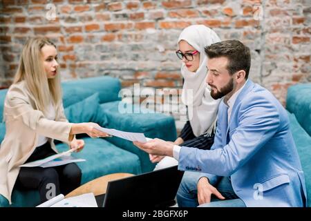 Pianificazione della strategia insieme. Gruppo multietnico di affari, donna musulmana, uomo e donna caucasica, tenendo e guardando la carta in cerca di un'idea Foto Stock