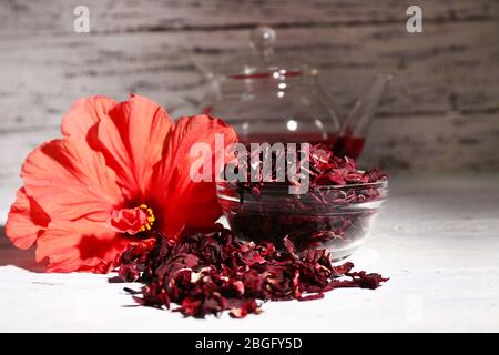 Tè Hibiscus in teiera di vetro e fiore su tovagliolo colorato su sfondo di legno Foto Stock