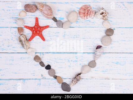 Cuore fatto da conchiglie e pietre su sfondo di legno Foto Stock