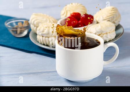 Caduta in una tazza di caffè. Su uno sfondo di legno azzurro. Lo zucchero di grumo cadde in una tazza con caffè e causò uno spruzzo di caffè. Foto Stock