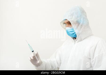 Vaccino contro il coronavirus, covid-19. Medico scienziato in tuta medica protettiva, rischio biologico, maschera facciale che tiene il vaccino in siringa. Vaccinazione Foto Stock