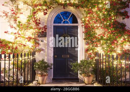 Porta anteriore di una casa incorniciata da una pianta di Pyracantha rampicante decorata con grappoli di bacche rosse e luci di Natale. Poundbury, Dorchester, UK, GB. Foto Stock