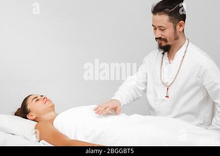 medico di medicina tradizionale orientale che fa un massaggio energetico senza contatto a una bella donna in un salone spa. Il massaggio energetico riprende il circolo Foto Stock