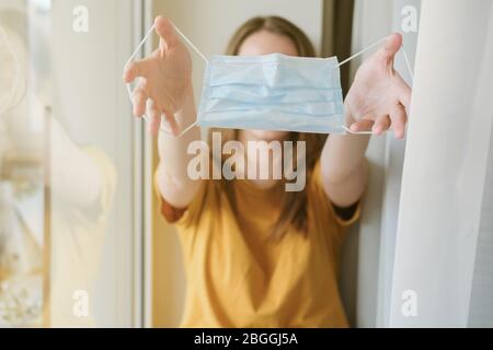 La ragazza tiene davanti a lei in mani estese della maschera medica del viso durante un coronavirus pandemico Covid-19. Isolamento a casa. Proteggetevi e. Foto Stock