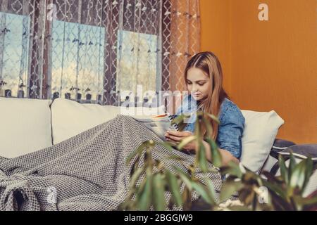 Ragazza seduta su un letto coperto con una coperta e studiare prima dell'esame, sta leggendo un libro e scrivendo note. Foto Stock