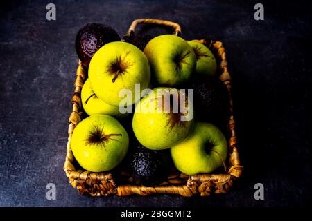 Mele e avocado in vimini piatto su superficie nera Foto Stock