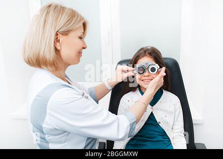 Ragazza mista di razza con telaio di prova optometristo in clinica di visione. Il medico femminile misura l'acuità visiva Foto Stock