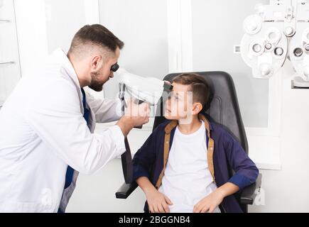 L'ottometrista maschile che fa esame visivo del paziente del ragazzo. Tonometro manuale per la misurazione della pressione intraoculare Foto Stock