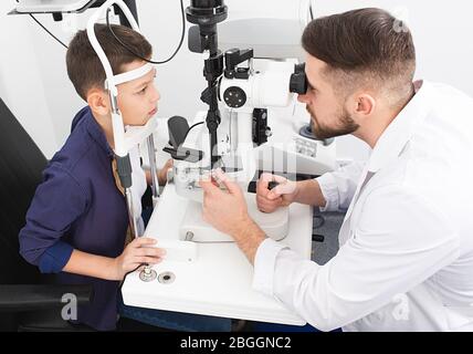 L'oftalmologo maschile controlla la vista di un ragazzo adolescente utilizzando una lampada a fessura binoculare. Controllo della vista nei bambini Foto Stock