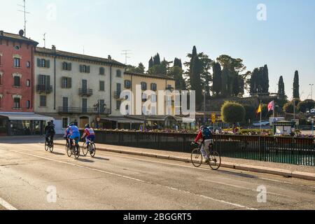 Un gruppo di ciclisti che passa sul ponte sul canale di mezzo nel centro storico di Peschiera del Garda, Verona, Veneto, Italia Foto Stock